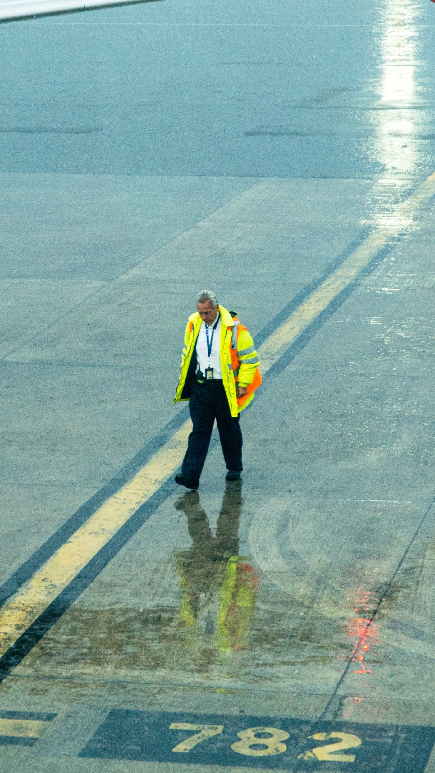 Ground crew member in reflective clothing walking on a rainy airport tarmac