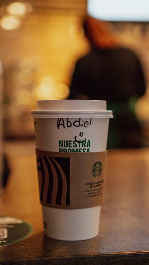 Free Close-up of a coffee cup with custom name inside a cafe. Warm lighting and cozy atmosphere. Stock Photo