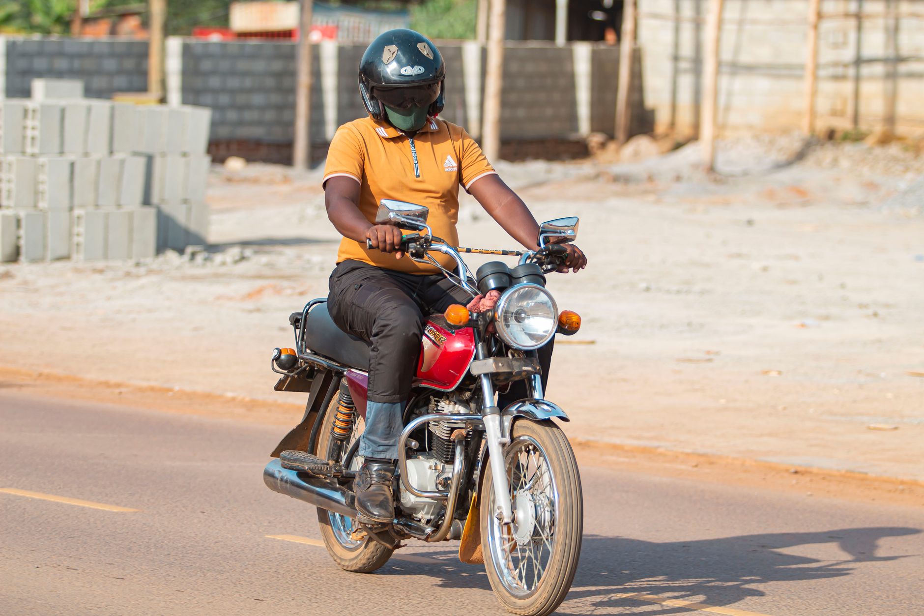 Motorbike rider wearing helmet on a sunlit urban street in Kampala, Uganda.