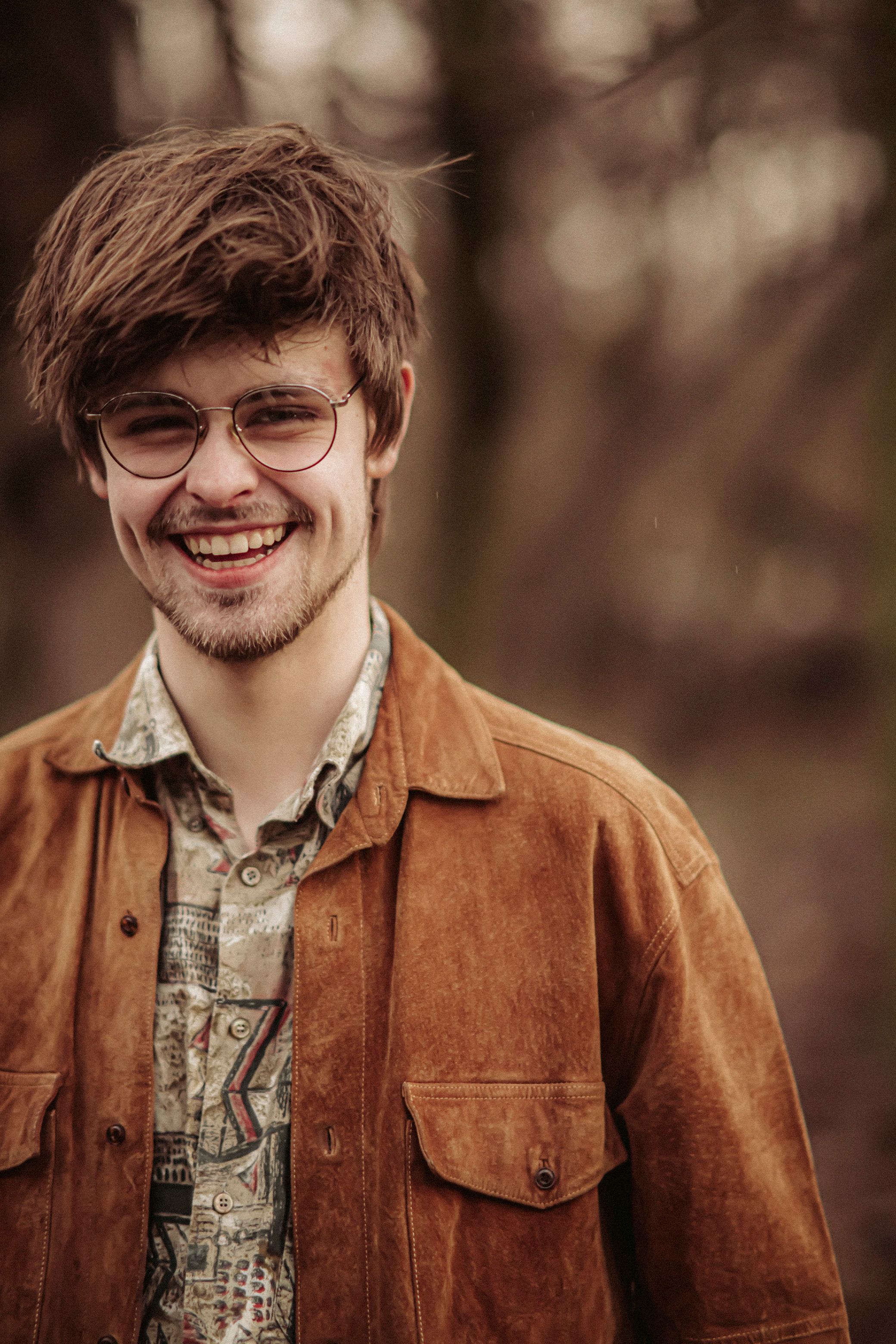 Portrait of a young man wearing glasses and a jacket in an autumn forest.
