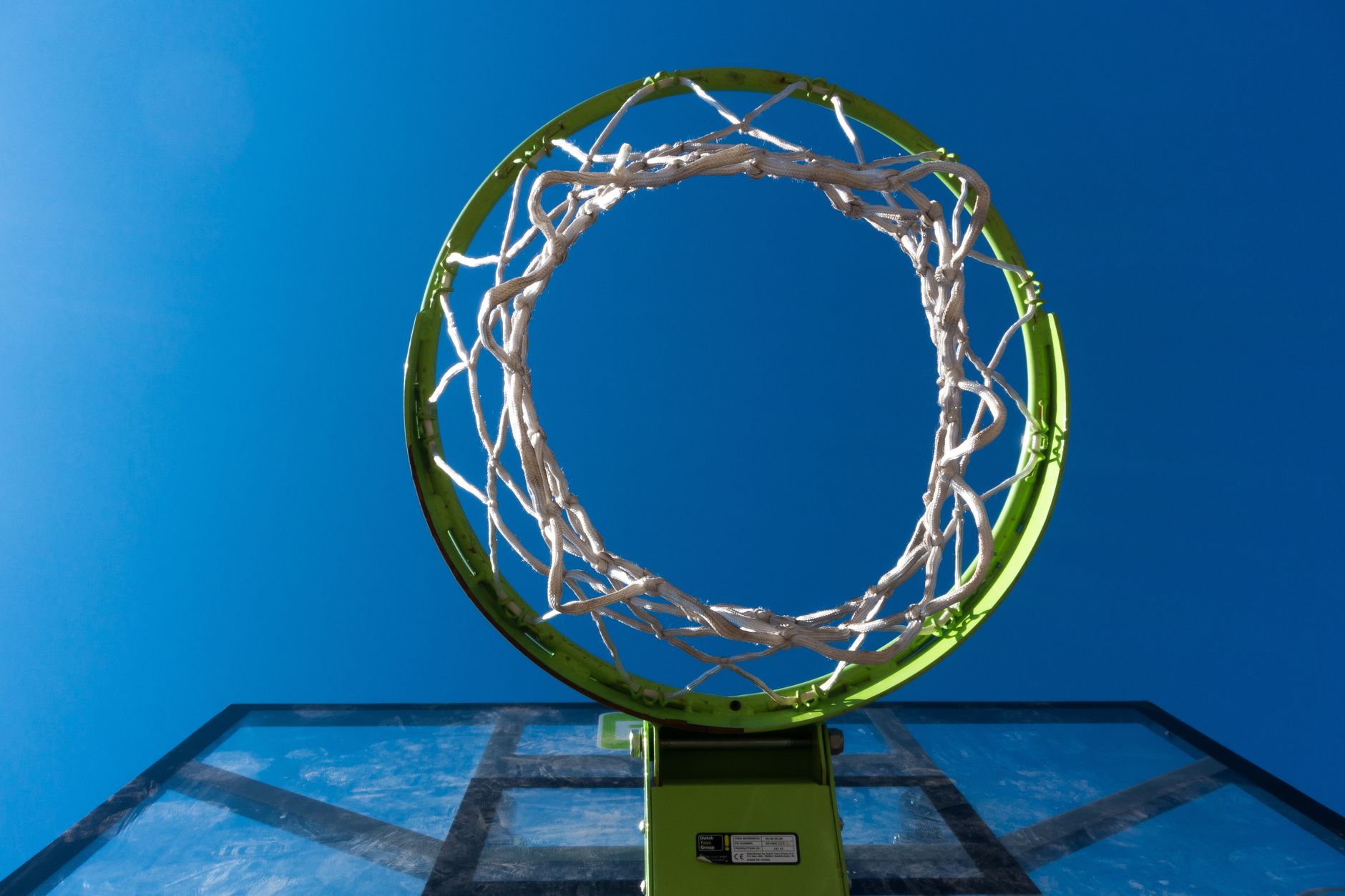 A view from below of a basketball hoop and net against a bright blue sky, symbolizing leisure and sports.