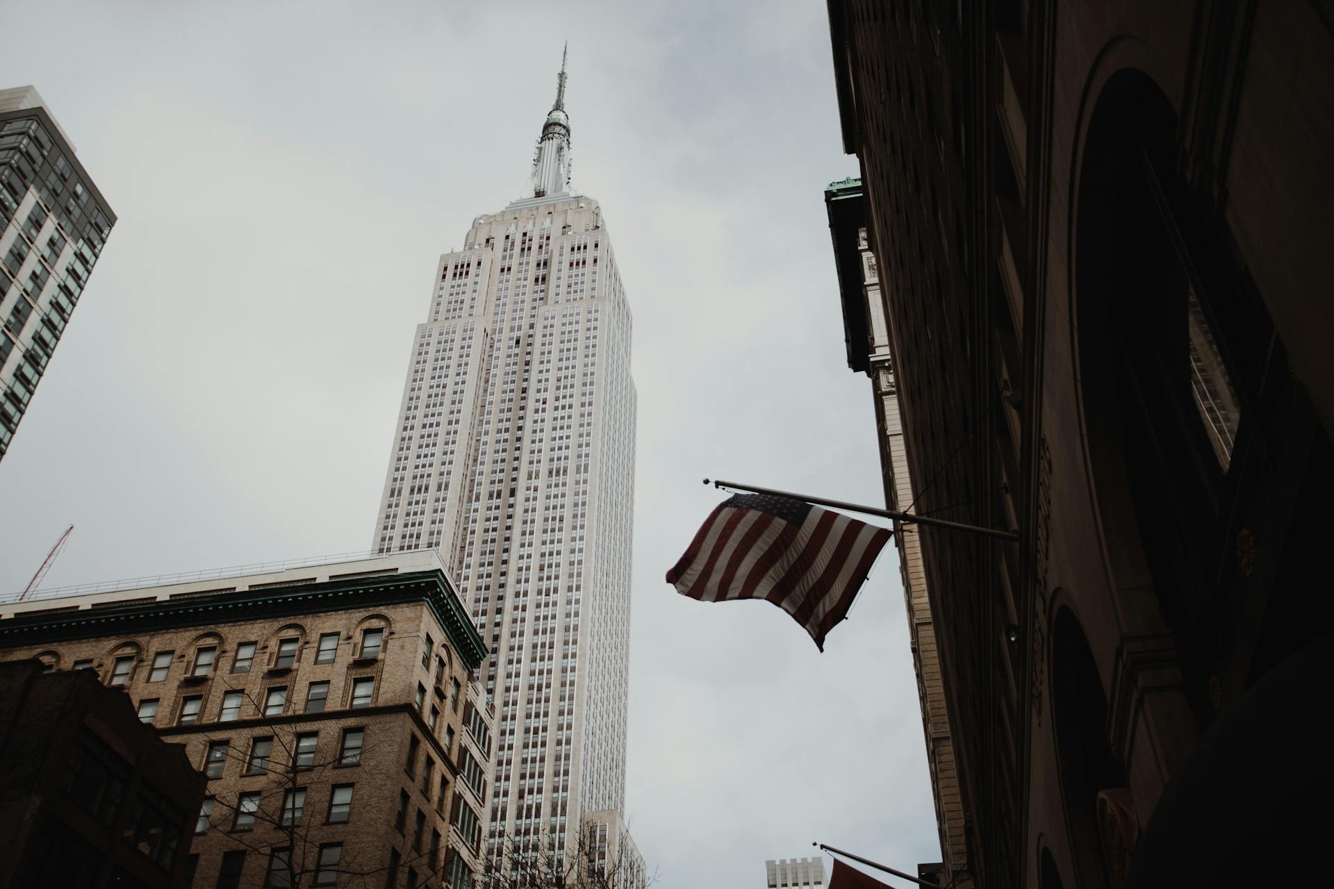 View of the Empire State Building with an American flag on a cloudy day.