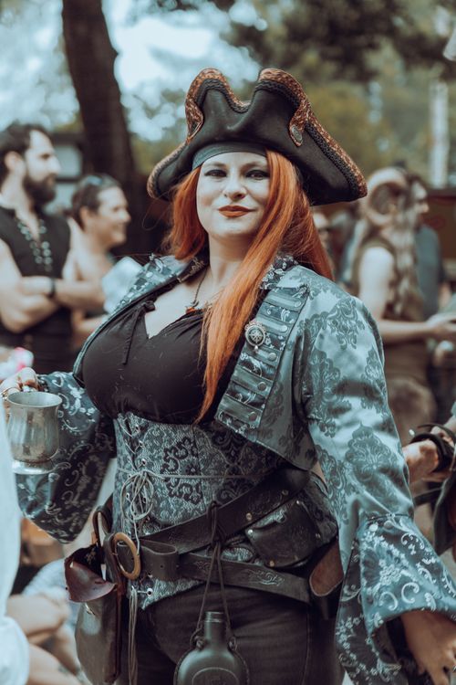 Free Woman in pirate costume posing at an outdoor festival, holding a metal mug. Stock Photo