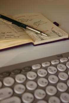 Detailed shot of a notebook with sketches, a pen, and a keyboard in view.