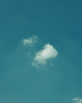 A tranquil blue sky featuring a single fluffy white cloud on a clear day.