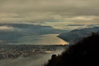 意大利特伦托的鸟瞰图，在多云的天空下，展现出一片薄雾笼罩的风景，其中有湖泊、山脉和村庄