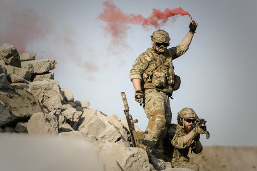 Two soldiers in camouflage, one signaling with red smoke in a desert setting.