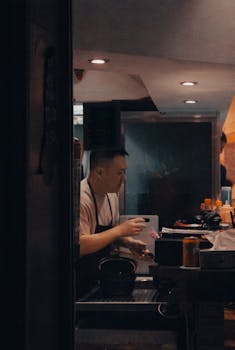 A chef wearing an apron is busy preparing a meal in a dimly lit kitchen at night.