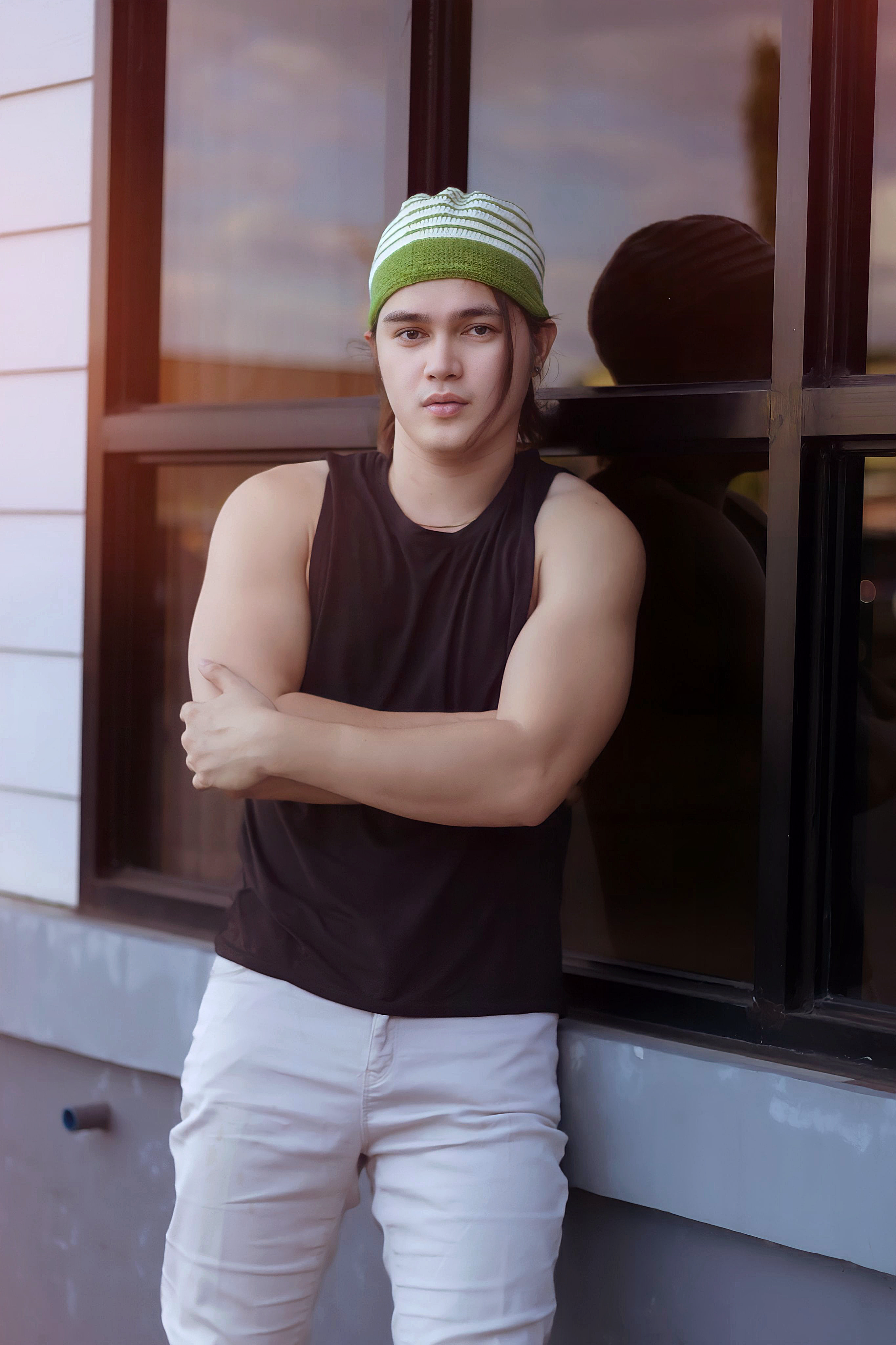 Confident young man in tank top and hat leaning against a building, exuding a relaxed fashion vibe.