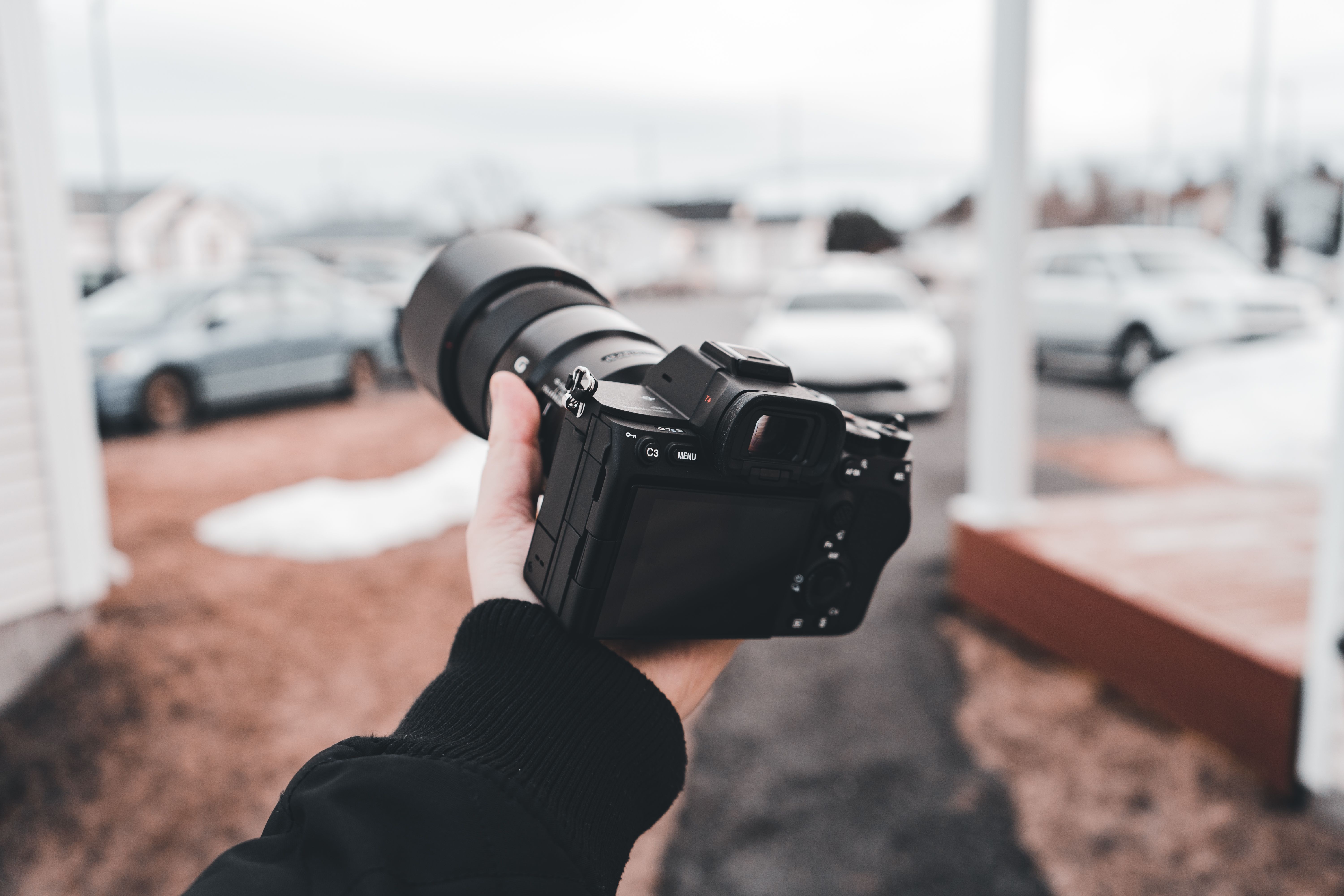 Close-up of a hand holding a camera with cars in the background on a cloudy day.