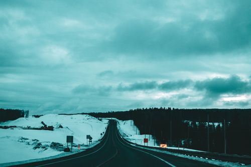 Free A long road stretches through a snowy landscape under an overcast sky in winter. Stock Photo