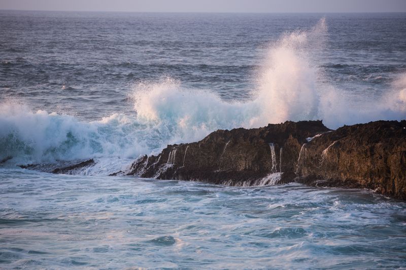Vibrant ocean waves crash against rocky coastline, showcasing nature's raw power.