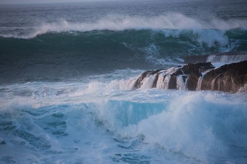 Free Powerful ocean waves crashing dynamically on a rocky shoreline under the clear sky. Stock Photo