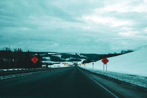 Free A serene winter road stretches under an overcast sky with snowy hills in the distance. Stock Photo