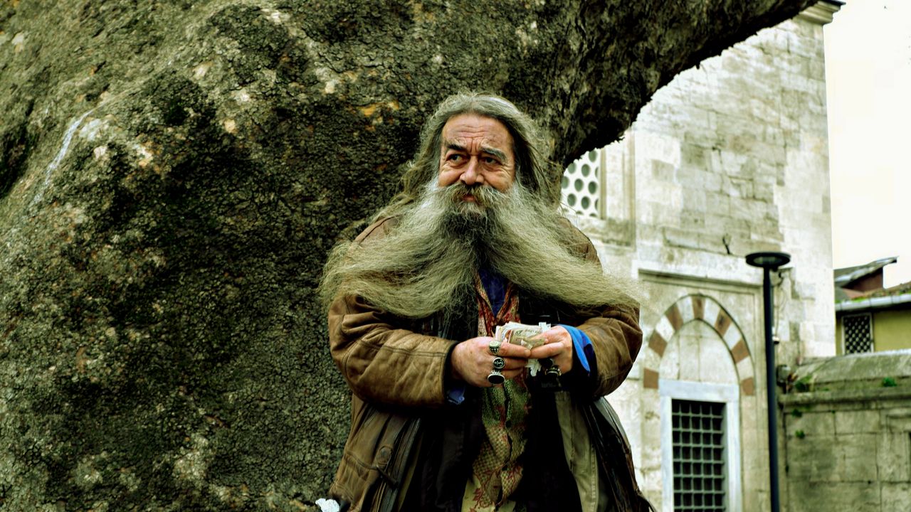 senior man with long beard holding item outdoors near historic stone s