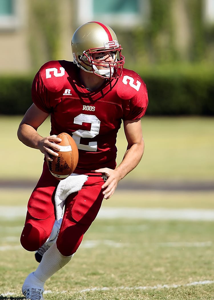 Football Player With Ball Running On Green Field During Daytime