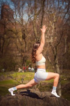 A woman in activewear practices yoga on a rock in Central Park's autumn scenery.