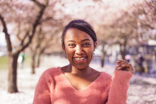 A joyful woman in a pink sweater smiles among cherry blossoms in Portland, Oregon.