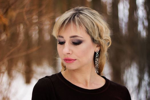 Close-up portrait of a young woman with elegant makeup and earrings in a natural outdoor setting.