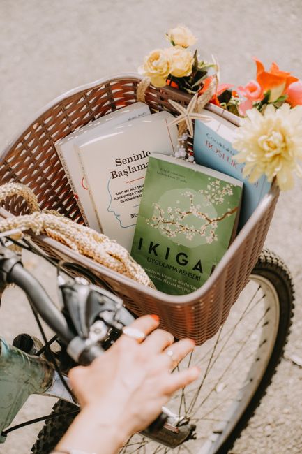 Decorative bicycle basket filled with books and flowers, held by a hand, symbolizing an artistic lifestyle.