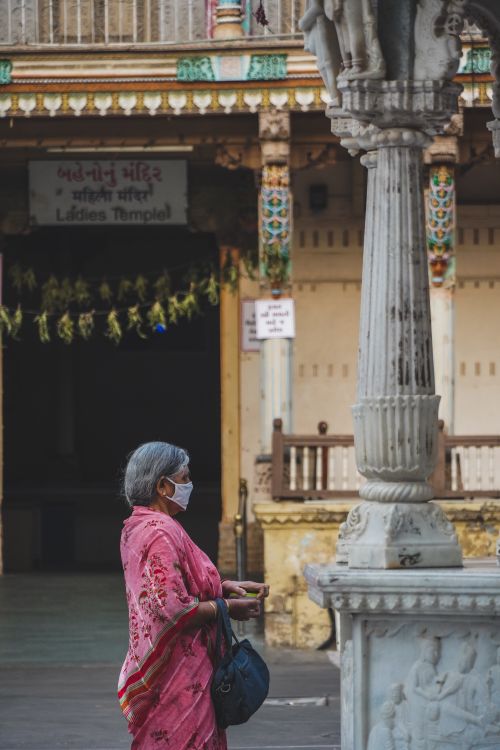 Free Elderly woman in traditional attire and face mask at Ahmedabad temple, capturing cultural and spiritual essence. Stock Photo