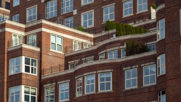 Detailed view of a red brick apartment building with terraces and greenery.