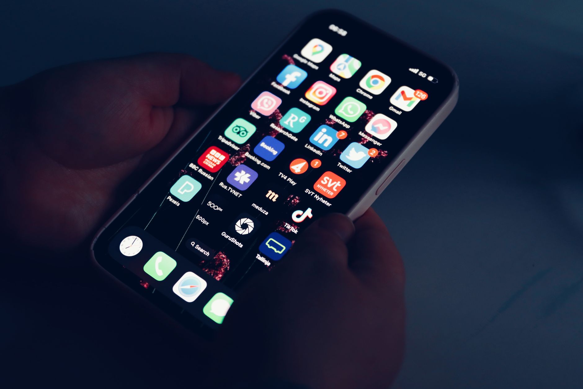 Close-up of hands holding a smartphone displaying various app icons in a dimly lit room.