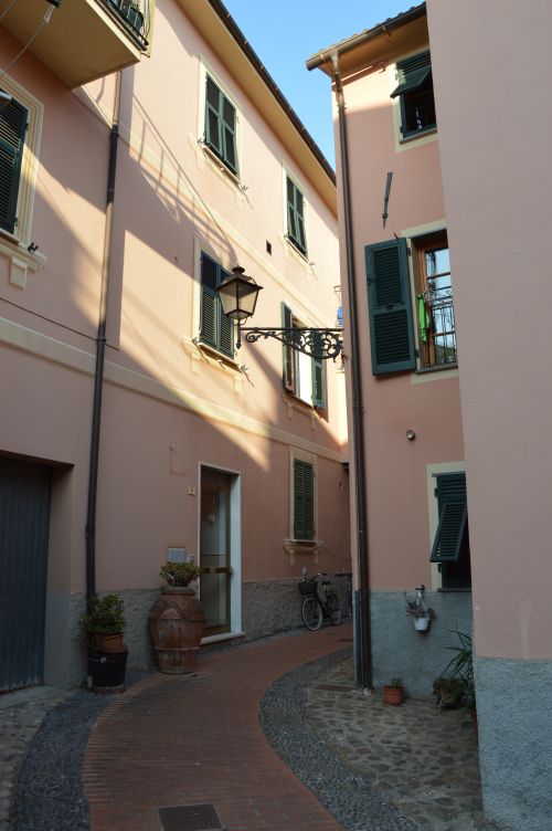 Free A quaint alleyway with pink townhouses and green shutters, featuring a bicycle parked nearby. Stock Photo