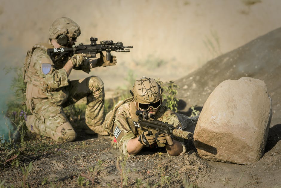Two soldiers in camouflage uniforms practice tactical maneuvers in a desert environment, exhibiting teamwork and precision.