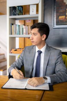 Elegant businessman in gray suit writing and working at modern office desk.