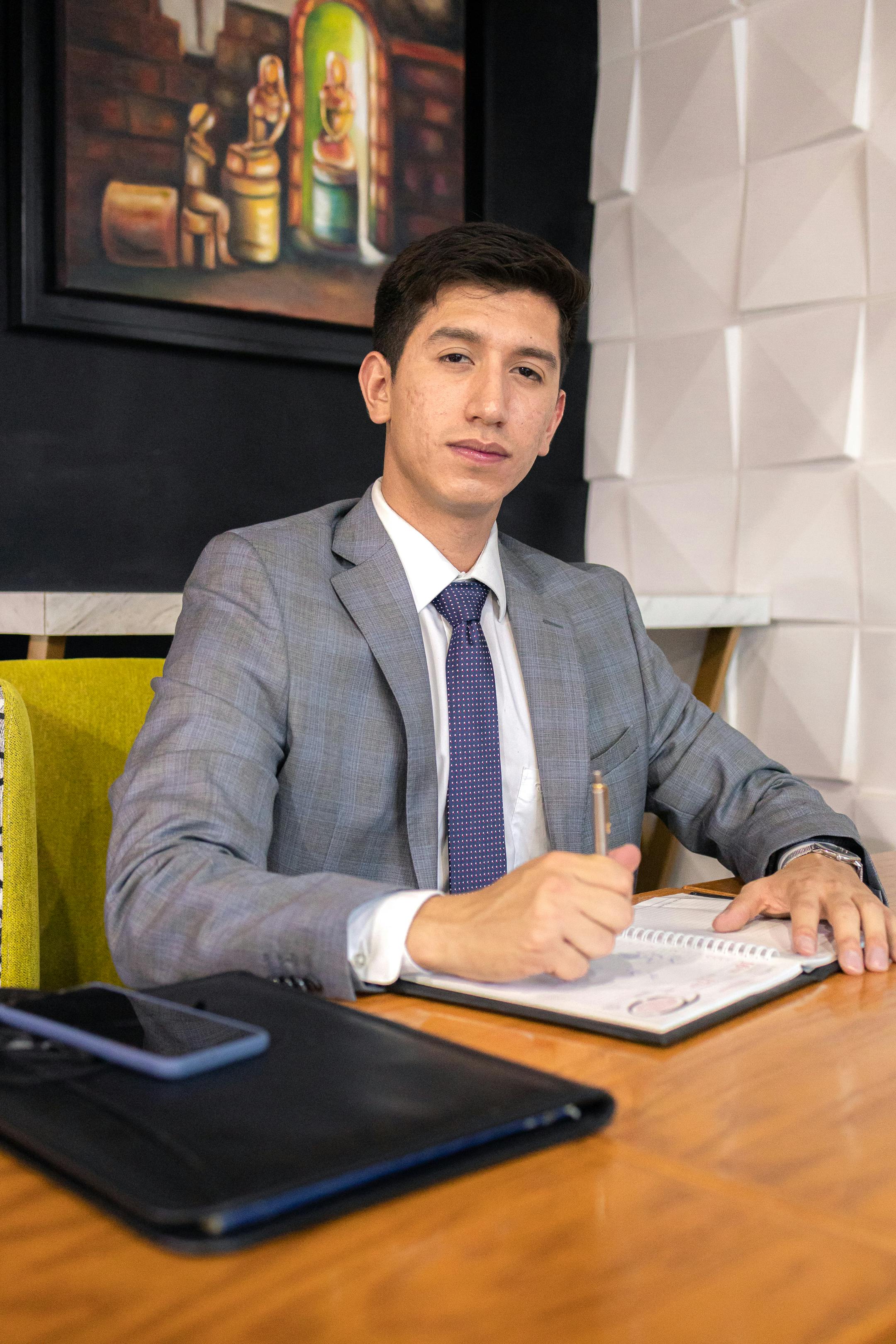 Professional businessman in a gray suit working at a desk with a notebook and pen.