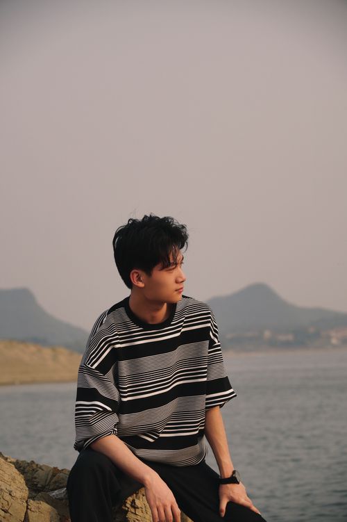 Free A young man with black hair gazes thoughtfully over a serene shoreline. Stock Photo