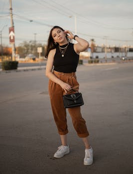 Stylish woman with long hair poses confidently in an empty parking lot holding a black handbag.