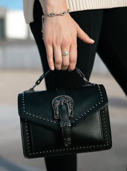 Close-up of a woman's hand holding a chic black handbag with stud details outdoors.