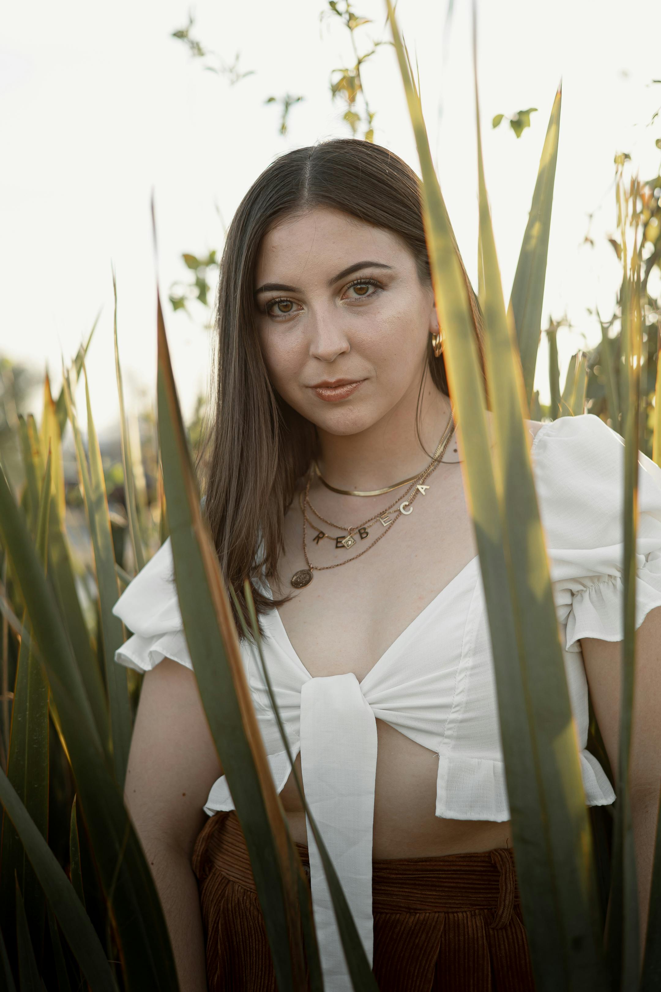 a woman in a white top and brown skirt standing in tall grass