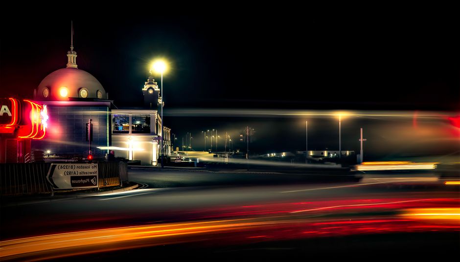 Nighttime urban scene with a dome building and light streaks on a city road.