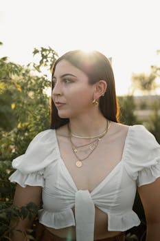 A woman in a white top stands outdoors, bathed in soft sunlight.