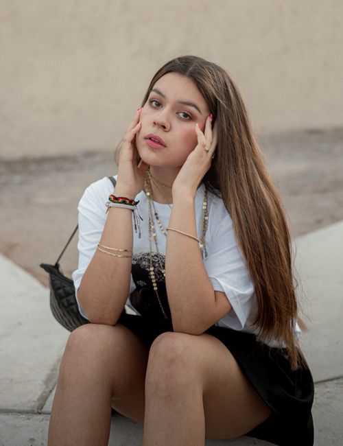 Free Young woman with long hair posing casually in an urban outdoor setting, showcasing modern fashion style. Stock Photo