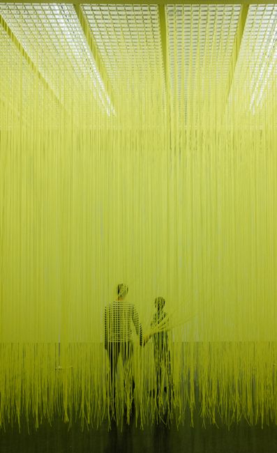 Couple immersed in vibrant yellow string art exhibit, Santa Cruz de Tenerife.