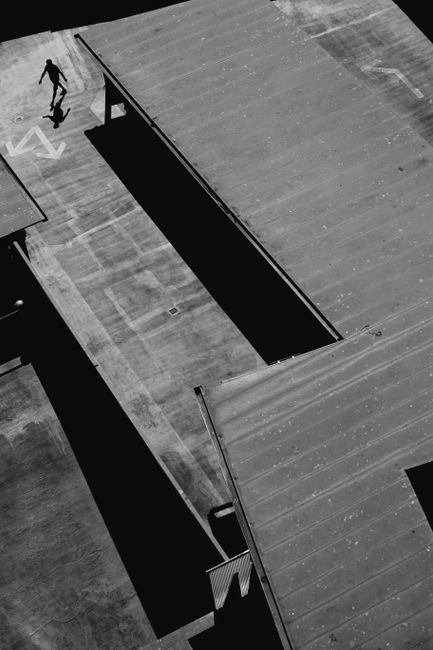 Aerial view of a solo figure exploring an urban rooftop in stark black and white contrast.