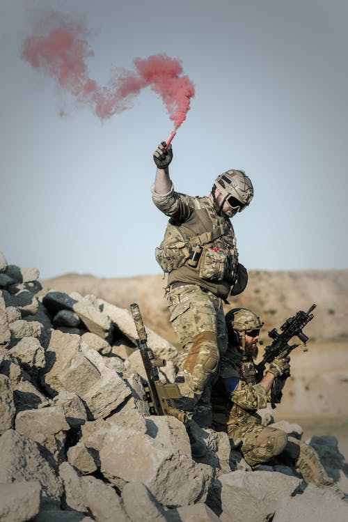 2 Soldado Com Armas Na Pilha De Pedras Cinza Segurando Um Bastão De Fumaça Durante O Dia