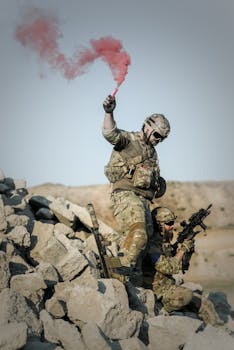 Soldiers in camouflage conduct a military operation using a red smoke signal.