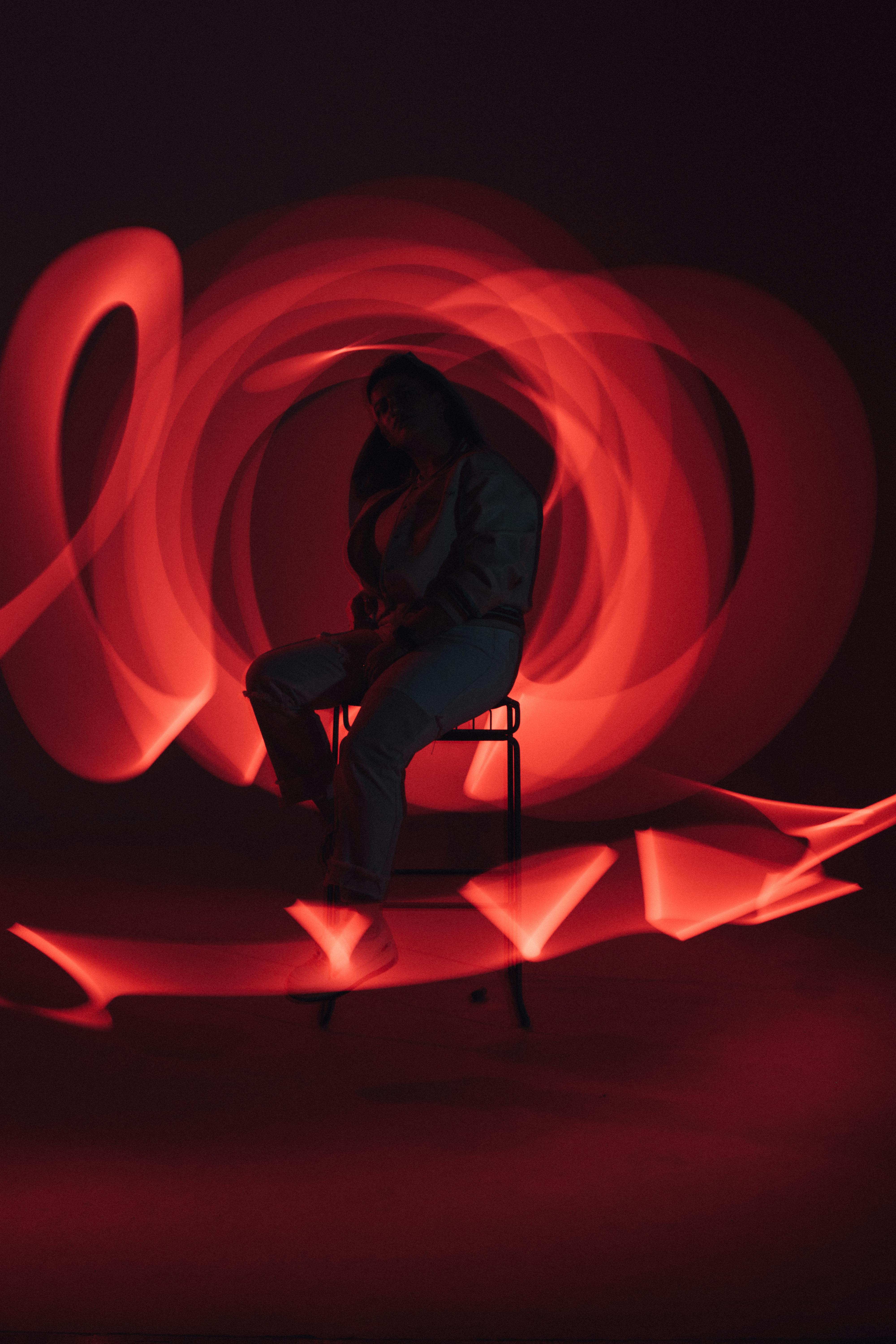 Silhouette of a woman sitting, surrounded by dynamic red light trails in a dark room.