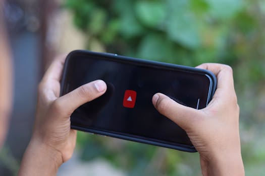 Close-up of hands holding a smartphone displaying a video app icon outdoors.