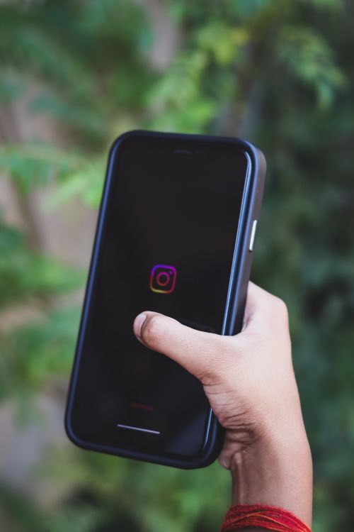 Free A close-up of a hand holding a smartphone displaying the Instagram app with a green background. Stock Photo