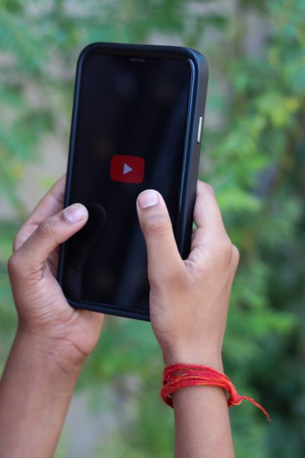 Close-up of hands holding a smartphone showing the YouTube logo outdoors. Close-up of hands holding a smartphone showing the YouTube logo outdoors.