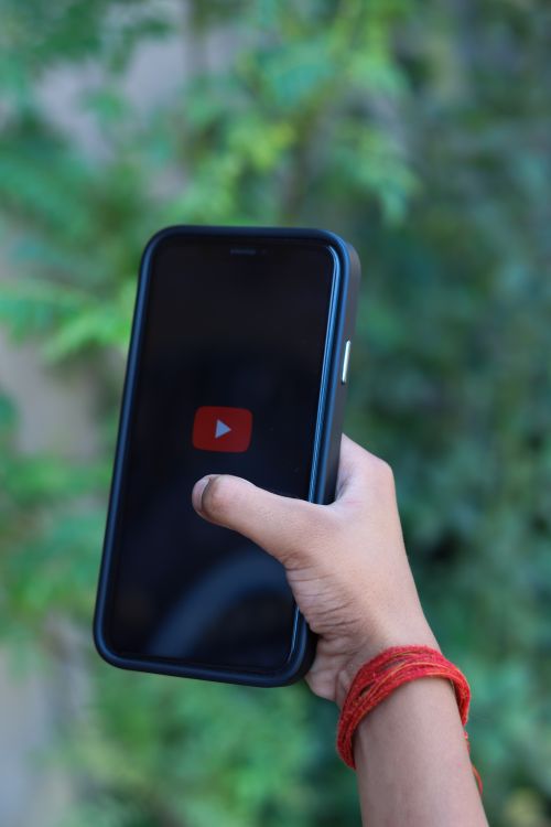 Free Hand holding smartphone with YouTube logo against a green background, outdoors. Stock Photo