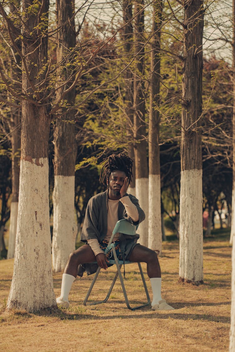 Photo Of A Young Man With Dreadlocks Sitting On A Chair Between Trees