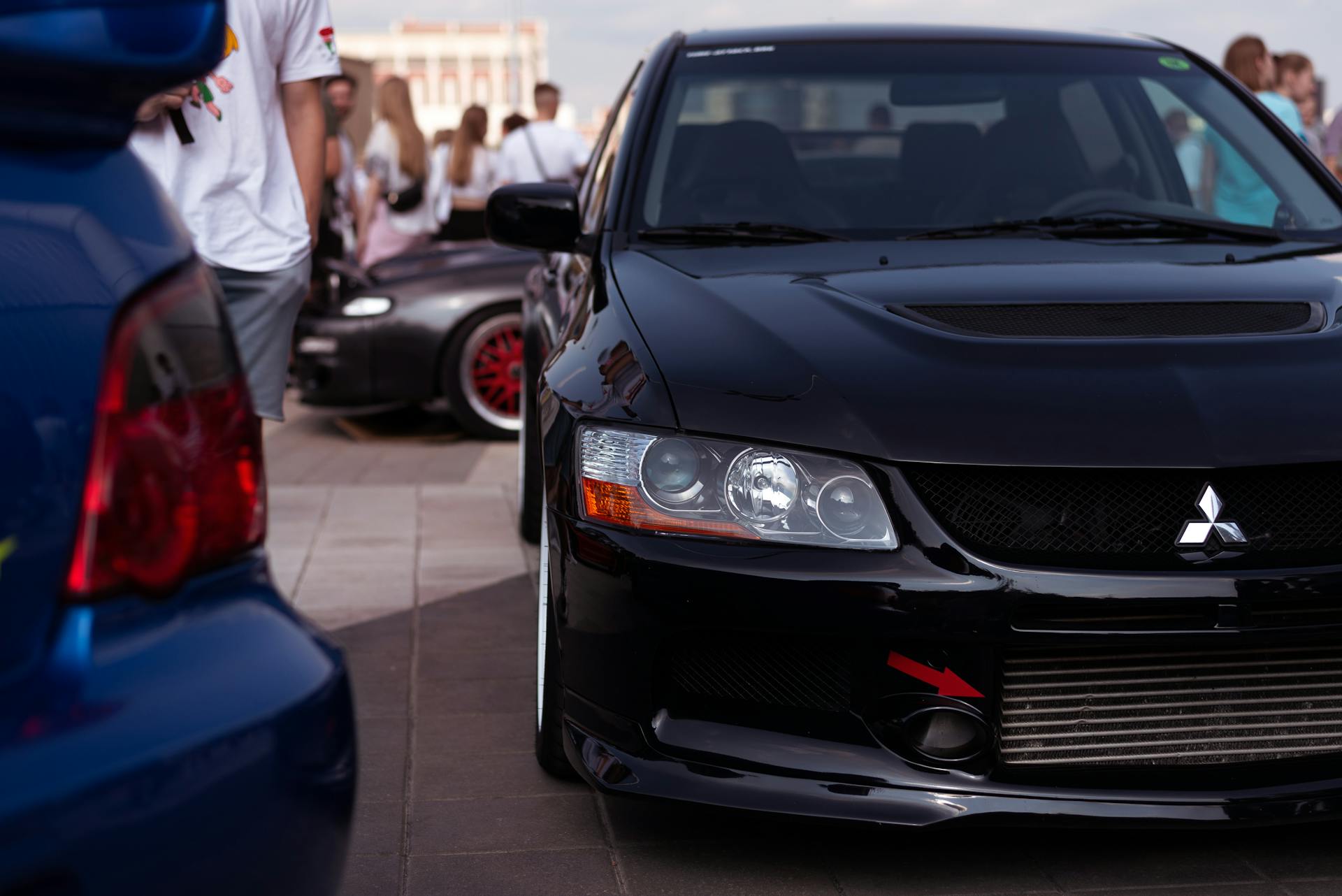 Sleek black car featured at an outdoor auto show with people in the background.