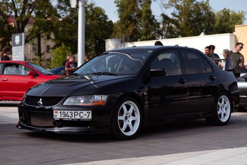 Free A sleek black Mitsubishi Lancer parked on urban pavement, surrounded by people and other cars. Stock Photo